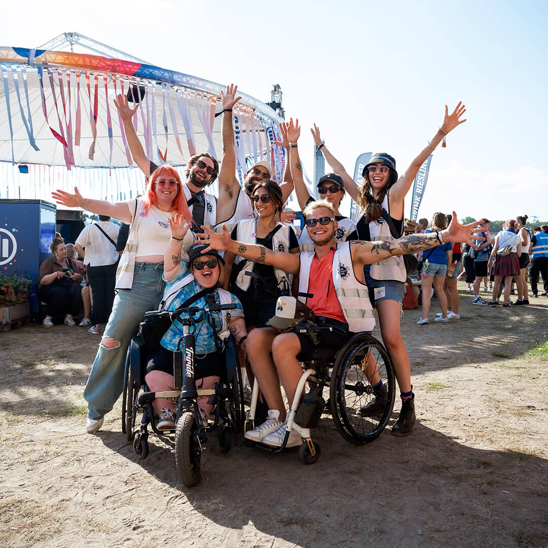 Teamfoto von 8 Mitarbeitenden auf dem Lollapalooza Festival 2024. Alle lachen und strecken fröhlich die Hände in die Luft.